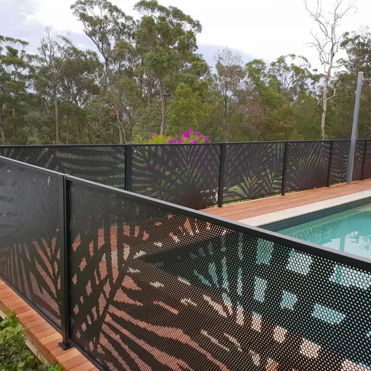 Black PoolPerf panels with the Palmy palm frond design around a raised pool, the sun throwing the pattern across the timber deck