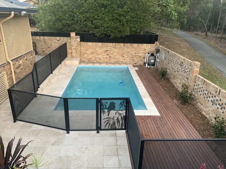 A black PoolPerf fence in Queensland that runs off a timber deck, down a step and across the paving to a gate, around a courtyard pool