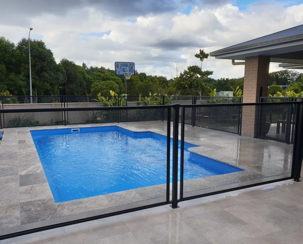 A bright blue pool in Queensland behind a black PoolPerf PurePerf fence, with the tiles, the water and the garden all visible through the panels